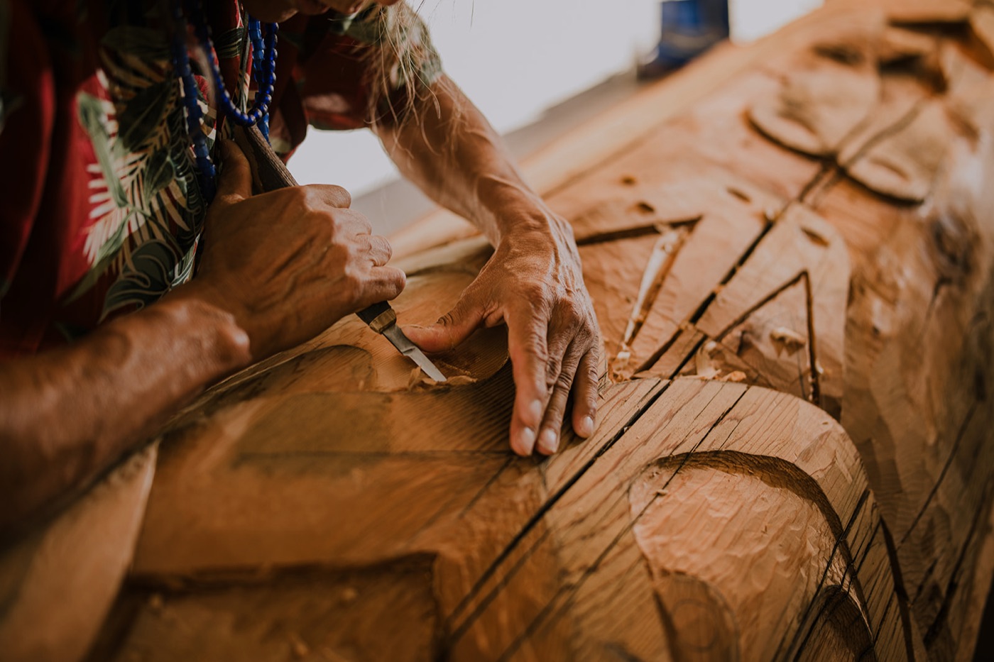 Hands carving a cedar pole.